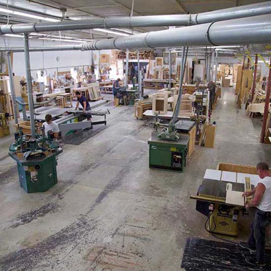 A spacious woodworking shop with multiple workers operating machinery and handling wood