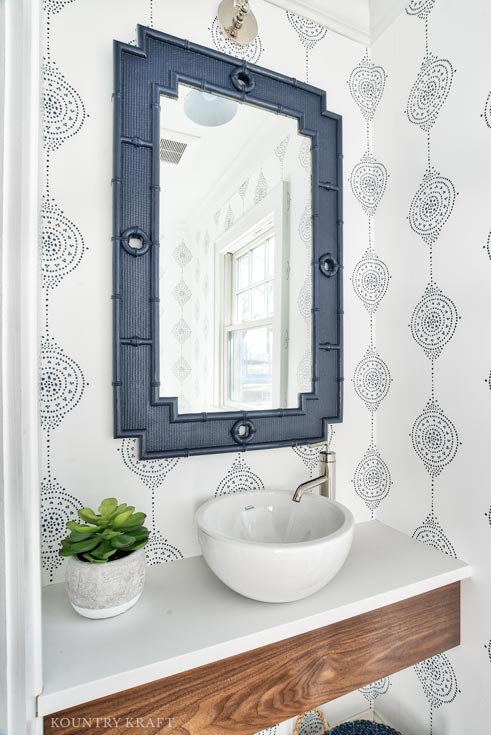 Rift cut what oak floating vanity in a Chatham, NJ powder room. White and blue patterned wallpaper, white vessel sink and mirror with thick navy frame.