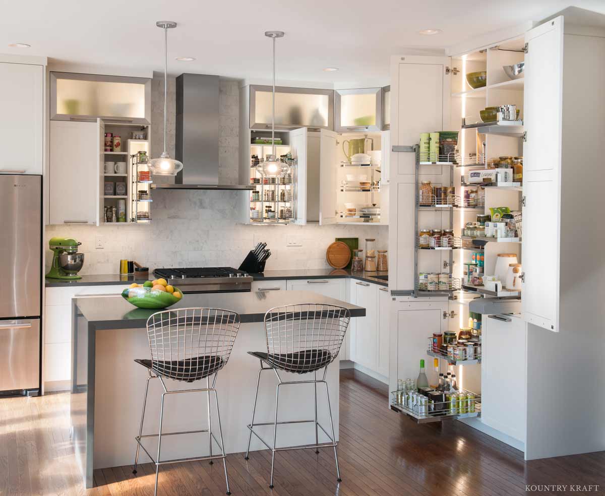 A white kitchen with doors open showing storage solutions with pull-outs and lighting.