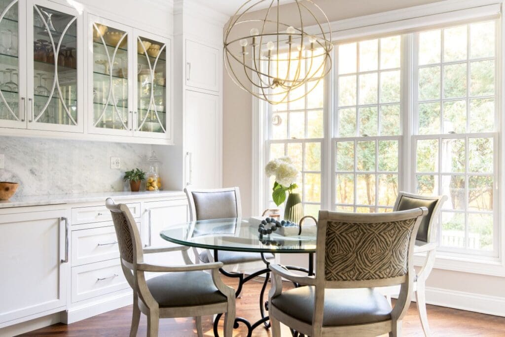 White custom dining room, built-ins featuring glass-front display cabinets with lighting, a marble countertop, and an integrated dining area with a glass table and geometric chairs.