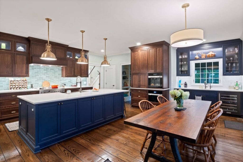 High end kitchen with a navy island, natural wood cabinetry, custom glass cabinets, brass pendant lighting, and built-in wet bar storage.