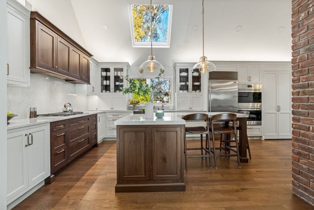 Two-tone custom kitchen cabinetry in New Jersey with a natural wood island, glass-front cabinets, skylight, and paneled storage for a high end kitchen design.