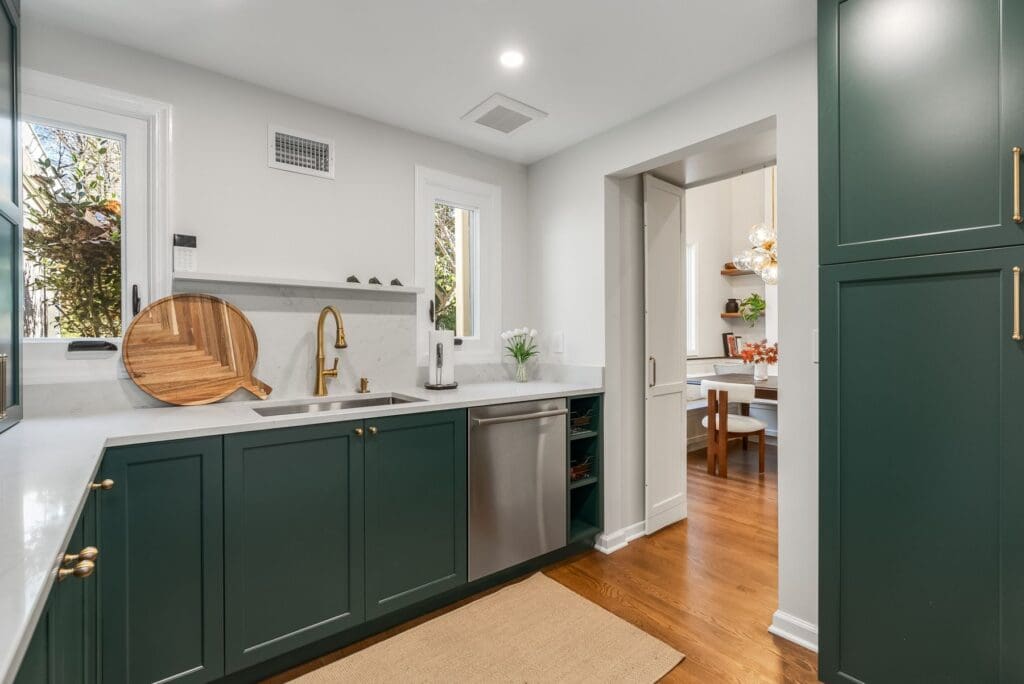 Back kitchen in Short Hills New Jersey with green custom cabinetry, brass hardware, quartz countertop, hidden pantry storage, and an integrated dishwasher.