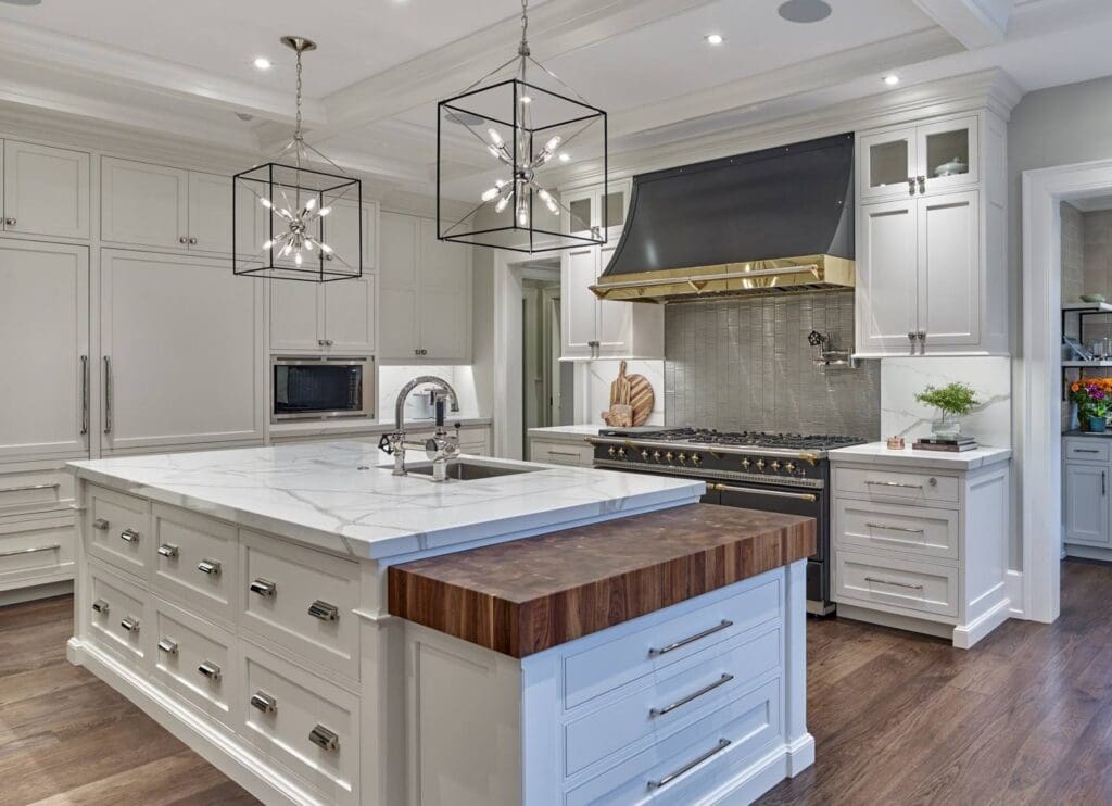 High end kitchen with a custom statement range hood, white inset cabinetry, walnut butcher block island detail, polished hardware, and full-height backsplash.